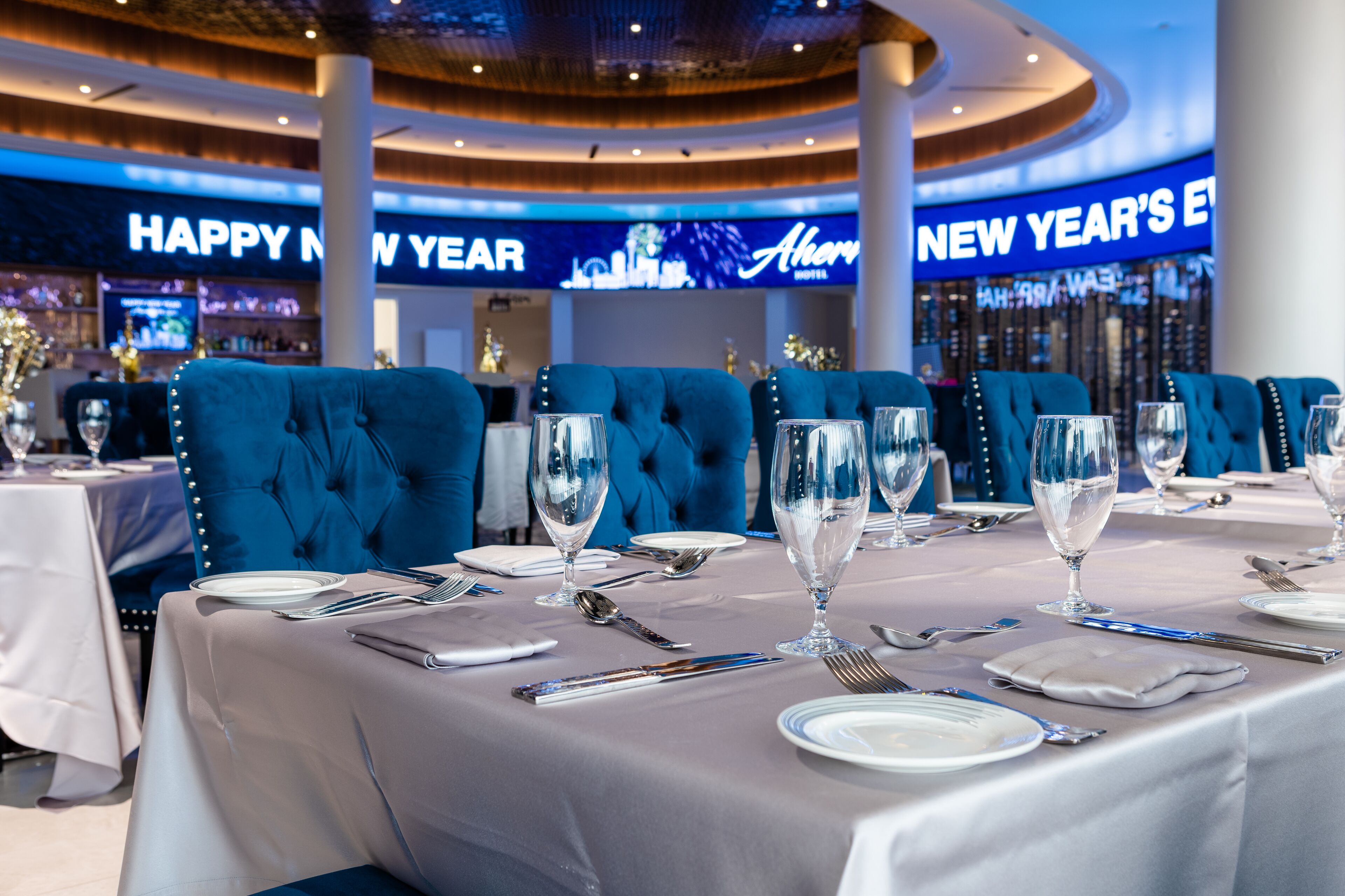 A restaurant with blue upholstered chairs and white tablecloths, a 'Happy New Year' sign, and a 'New Year's Eve' sign in the background.