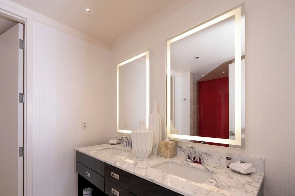 Une salle de bain moderne avec un lavabo en marbre, deux grands miroirs et une zone de douche carrelée de carreaux rouges.