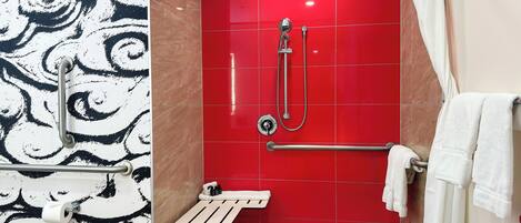 Un baño con pared de azulejos rojos, una ducha con cabezal de ducha manual, un perchero para toallas y un dispensador de papel higiénico.