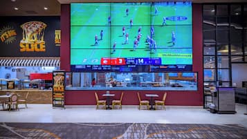 Un bar esportiu amb una gran pantalla que mostra un partit de futbol, zones d'asseu-se i un anunci de pizza.