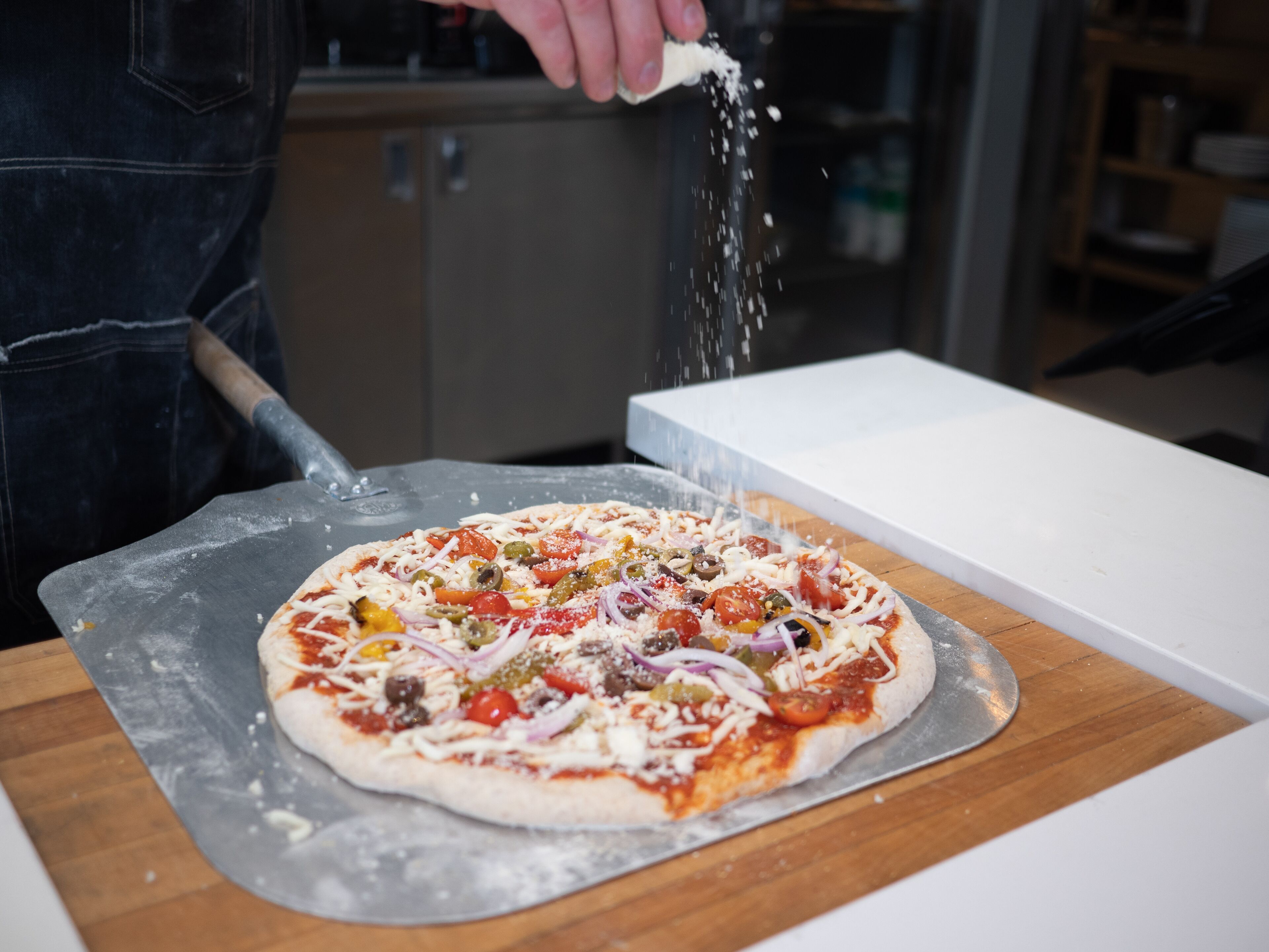 Pizza en bandeja metálica con distintos ingredientes, espolvoreada con queso.