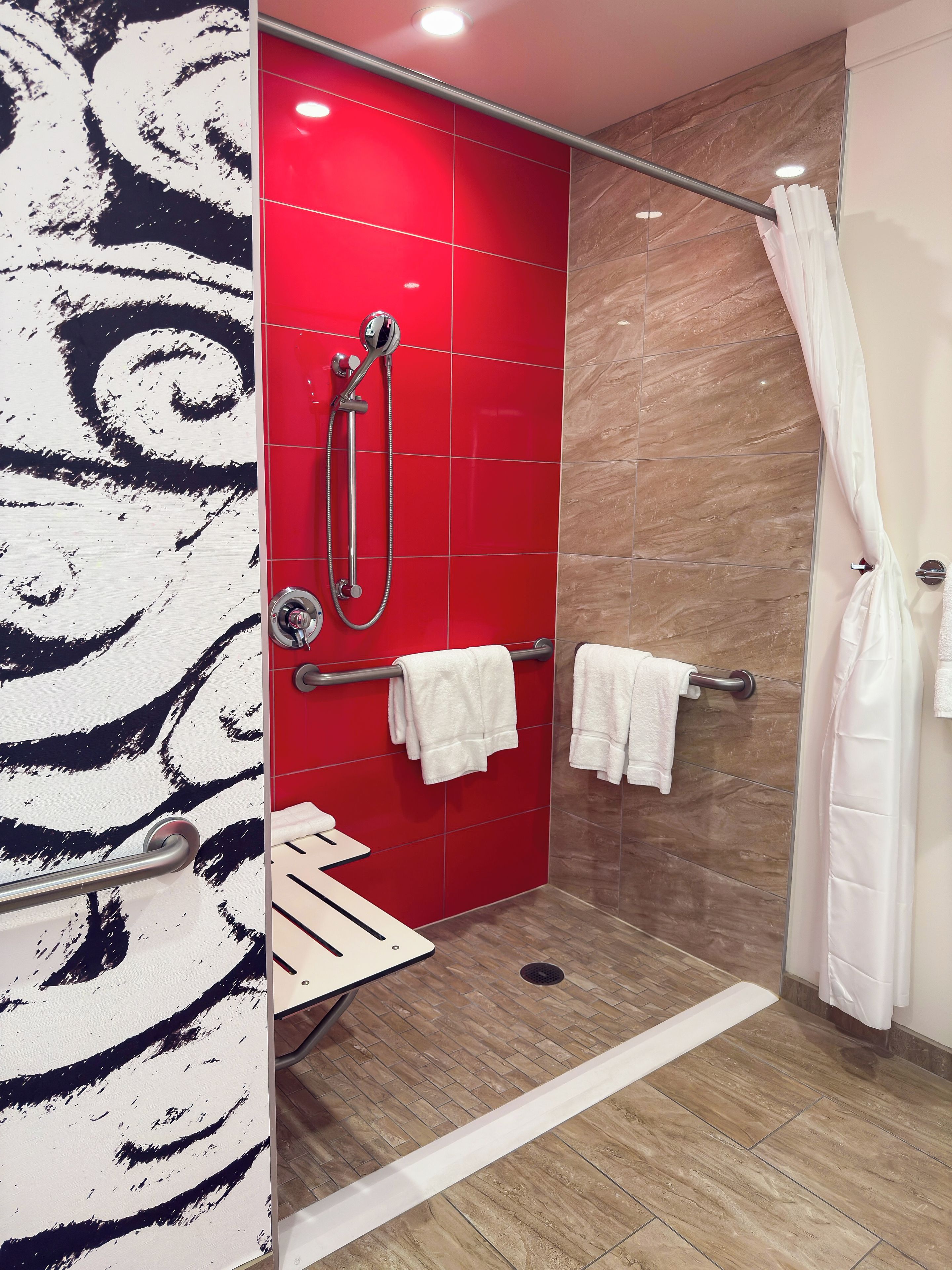 A modern bathroom with a red tiled shower wall, a glass shower door, and a white towel rack.
