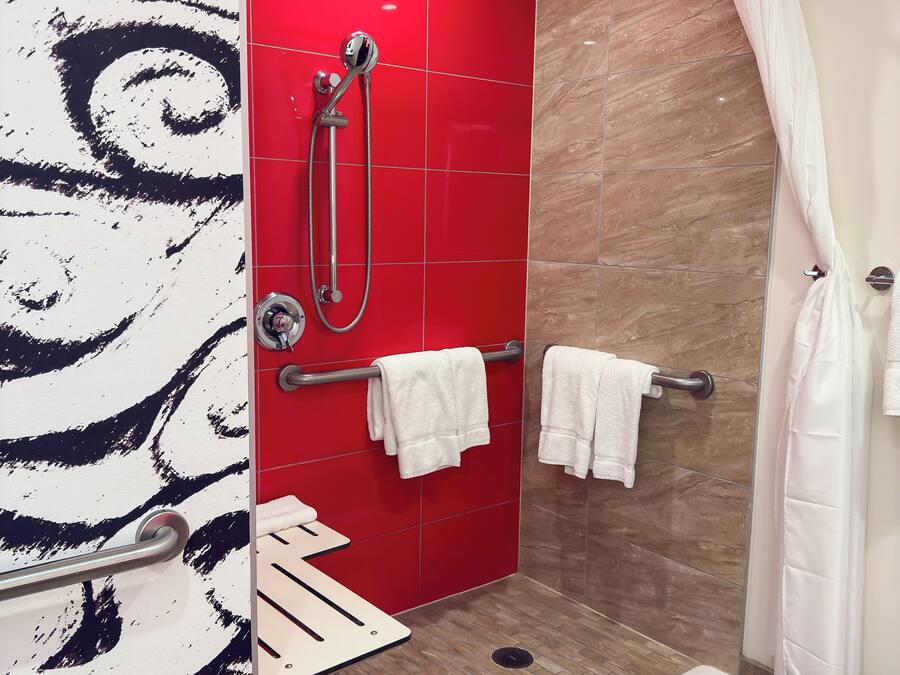 Een moderne badkamer met een rode betegelde douchewand, een glazen douchedeur en een witte handdoekhouder.