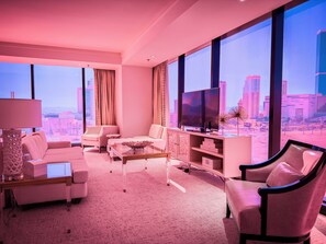 Een moderne woonkamer met uitzicht over de stad, met een bank, fauteuils, een salontafel en een tv op een kast.