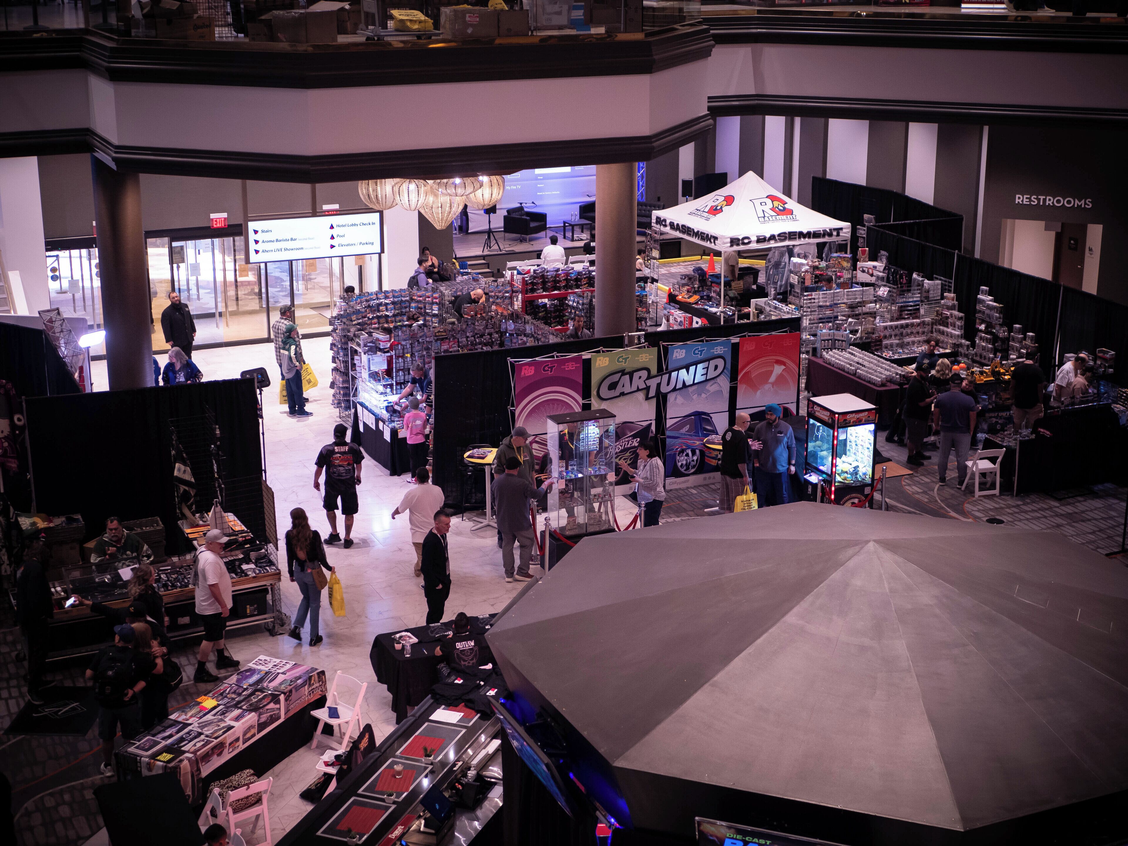 Ein Kongresszentrum mit verschiedenen Ständen und Ausstellungen, darunter ein 'Cartuned'-Stand und ein 'DIECAST'-Schild.