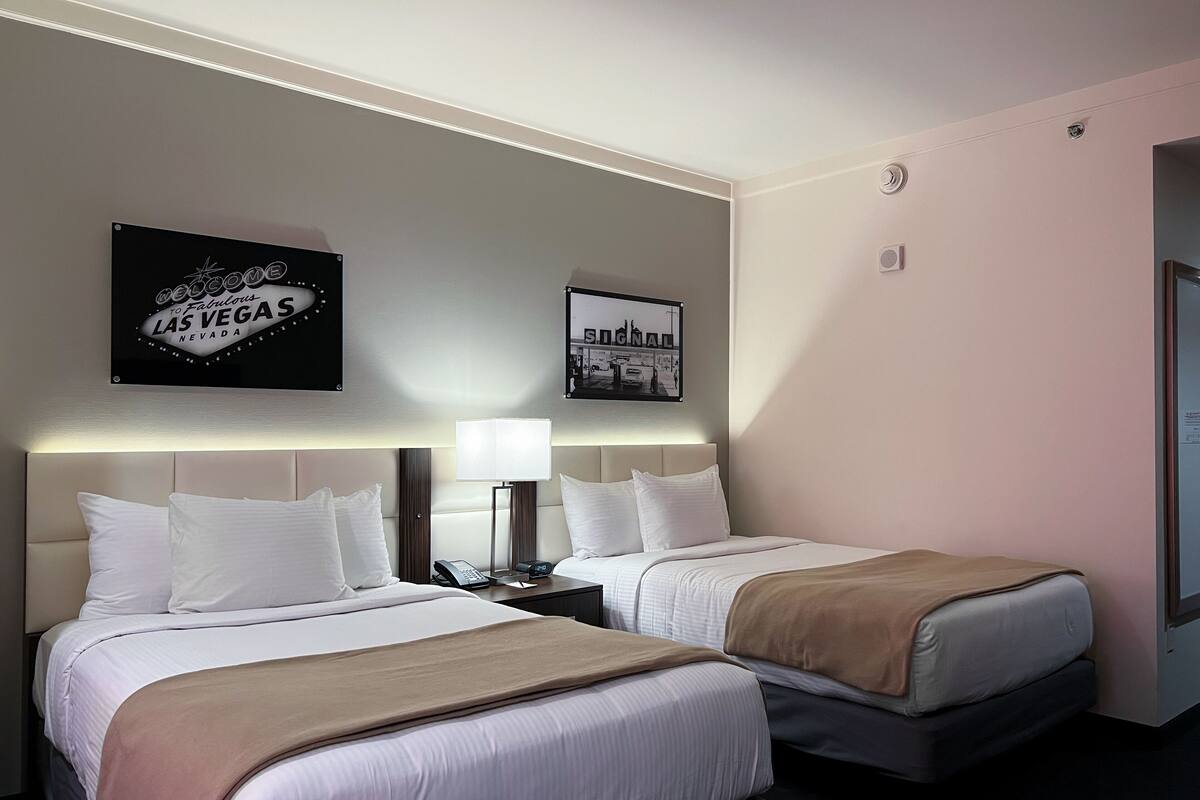 Une chambre d’hôtel avec deux lits, une table de chevet avec une lampe, un téléphone et un tableau encadré au mur.