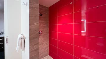 Un baño moderno con una puerta blanca, un perchero, una ducha con pared roja y piso de baldosas.