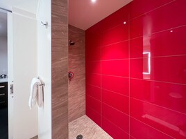 Un baño moderno con una puerta blanca, un perchero, una ducha con pared roja y piso de baldosas.