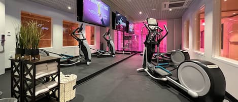 Une salle de sport équipée de matériel d’exercice, d’un écran de télévision et d’un mur sur lequel est affiché un panneau.