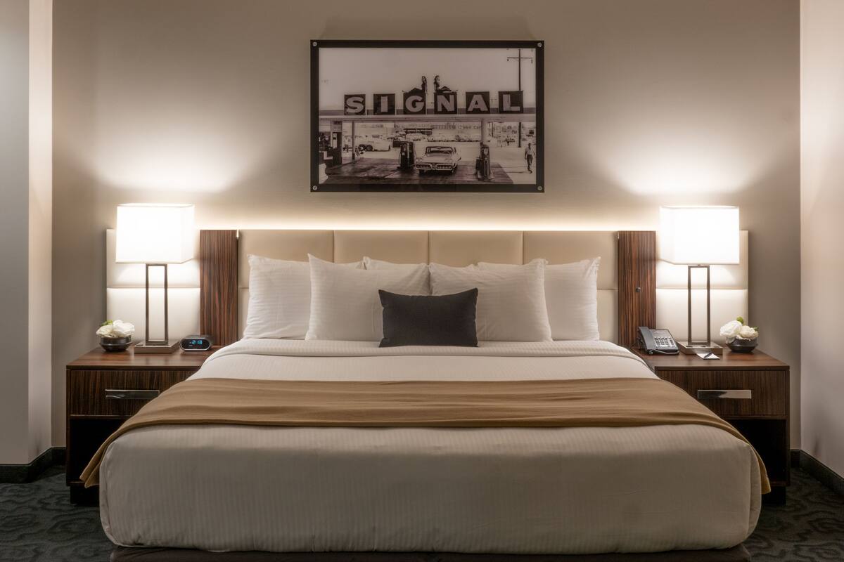 Une chambre d’hôtel avec un grand lit, deux tables de chevet, une petite table, un tableau encadré au mur et deux lampes.