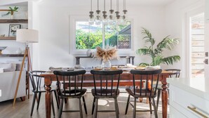 A dining area with a wooden table and chairs, a hanging light fixture, and a window with a view of greenery. - Wine Country Escape, Heated Pool + Hot Tub Near Wineries (Santa Rosa)
