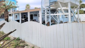 Une maison située sur la côte, avec une façade bleue, une clôture blanche et un escalier bleu menant à un balcon.