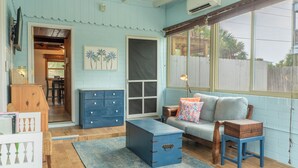 Une pièce chaleureuse avec un mur bleu, une malle en bois, un canapé et une fenêtre donnant sur des palmiers.