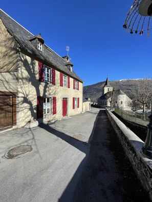 Une rue étroite, bordée de bâtiments des deux côtés, un mur de pierre et un ciel bleu dégagé.