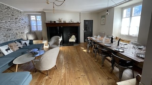 Een gezellige woonkamer met een stenen muur, een open haard, een eethoek met een houten tafel gedekt voor zes personen, en een blauwe bank.