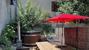 Een houten picknicktafel met banken, een rode parasol en een houtkachel in een achtertuin.