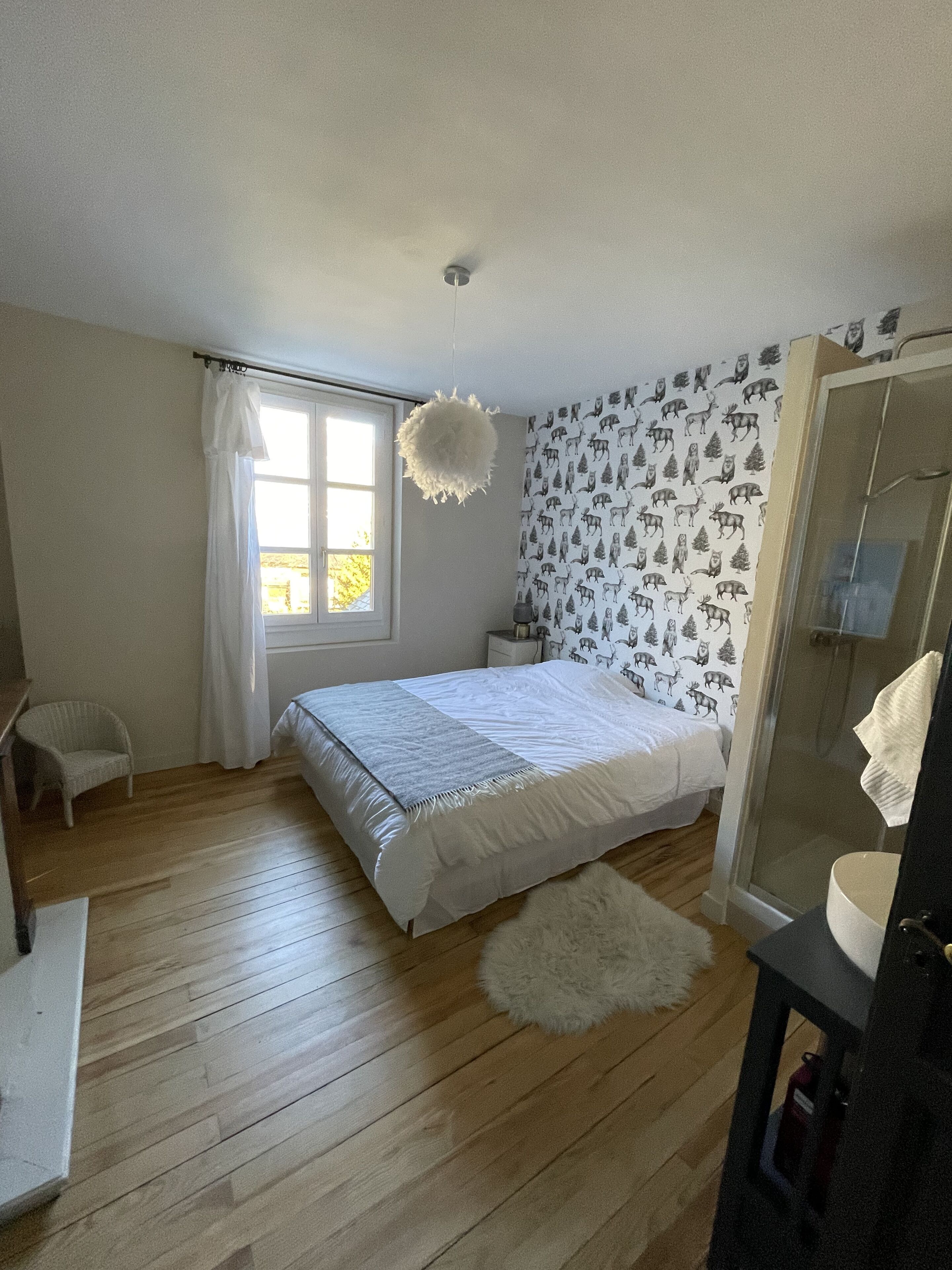 A bedroom with a bed, a window, a shower, and a patterned wall.