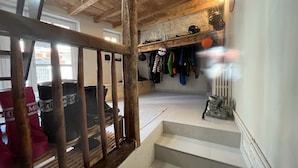 Een houten trap die leidt naar een kamer met een witte muur en een plank met diverse spullen.