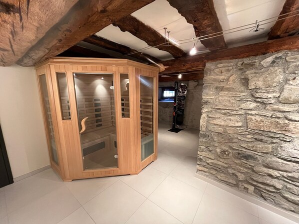 Un meuble en bois doté de portes en verre, un mur en pierre et un plafond avec des poutres apparentes.