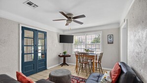Una habitación con una mesa de comedor, sillas, un ventilador de techo, un televisor y una puerta.