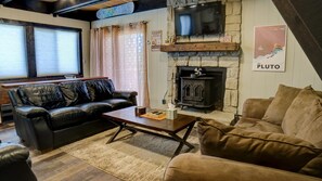A cozy living room with a fireplace, leather sofas, a television, and a ski-themed poster. - Cozy home near the Deer shuttle stop (Angel Fire)