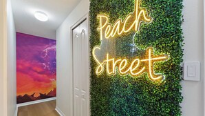 A hallway with a neon sign reading "Peach Street" and a wall covered in green foliage. - Private Pool, Premium Resort Amenities Included (Kissimmee)