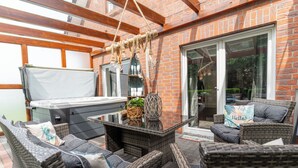 Eine Terrasse im Freien mit Korbmöbeln, einem Tisch mit Glasplatte und einem Grill.