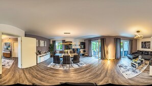 Ein weiter Blick in ein modernes Wohnzimmer mit Essbereich, einer Sofagarnitur und einem großen Fenster mit Blick ins Freie.