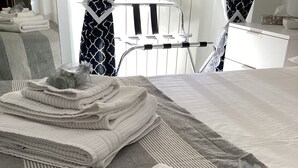 Toallas blancas dobladas ordenadamente sobre una alfombra gris, una botella de vidrio con jabón y una silla con cortina de diseño blanco y negro al fondo.