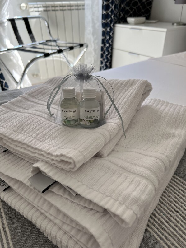 A neatly folded white towel on a bed with two bottles of B.Natural shampoo and body wash. - VICOLO CORTO Historic Center: Relax & Work from Home (Velletri)