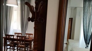 Una habitación con comedor que incluye una mesa y sillas de madera, un espejo grande y una cama con cortina estampada.