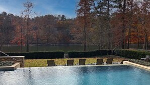 Ein Pool mit Liegestühlen und Blick auf einen von Bäumen umgebenen See.