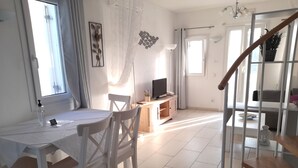 A bright room with a dining table, chairs, a TV, and a staircase. - Sea paradise villas (Santorini)