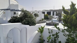 A white-walled building with a flat roof, outdoor seating area, and greenery. - Sea paradise villas (Santorini)