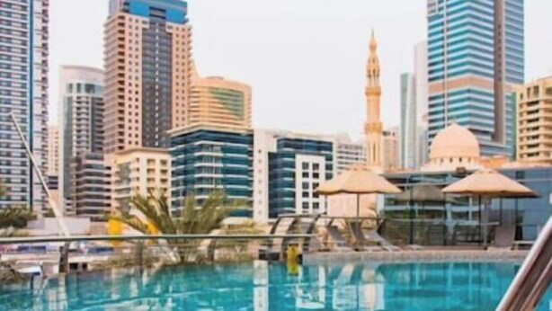 A swimming pool with a cityscape in the background, including modern high-rise buildings and a mosque. - Signature Hotel Dubai Marina (Gillingham)