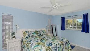 A bedroom with a bed, a ceiling fan, a window with blinds, a bedside table with a lamp, and a mirror. - Beautiful Florida Home 3 Miles to Venice Beach (Venice)