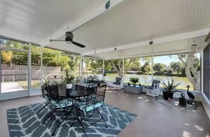 A covered patio area with a dining table and chairs, surrounded by potted plants and a view of a lake. - Beautiful Florida Home 3 Miles to Venice Beach (Venice)