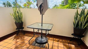 A tiled patio with a table and chairs, surrounded by potted plants and palm trees. - Escape Beach Studio, Fairway Courts, Palmas del Mar (Humacao)