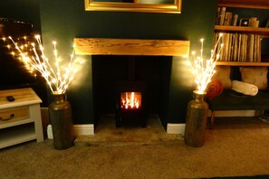 A fireplace with a wooden mantel, flanked by two vases with lighted candles, a bookshelf with books, and a television on a wooden stand. - Quirky cottage with 3 bedrooms & a hot tub (Bradford)