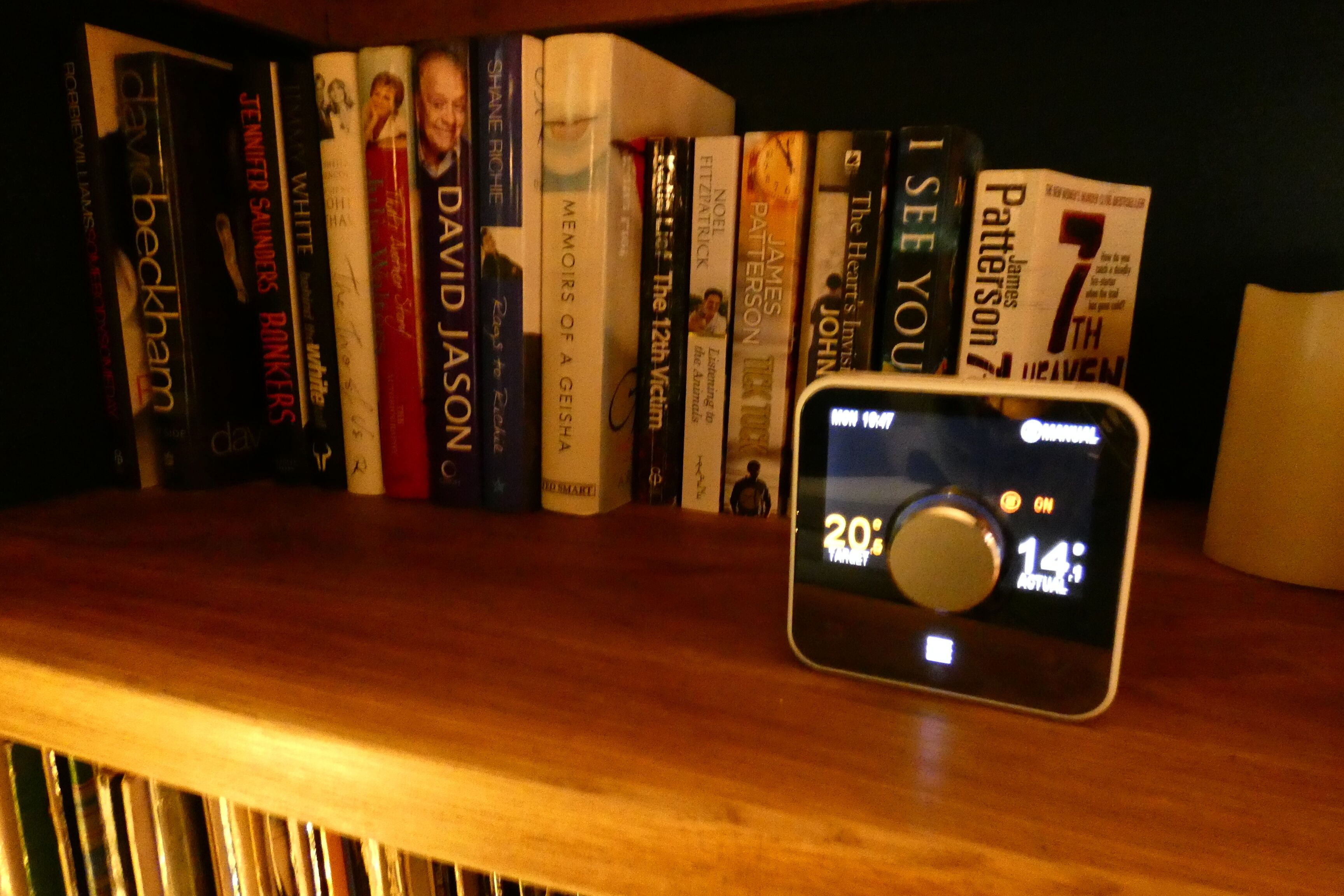 A wooden bookshelf with books and a digital clock displaying 20:14.