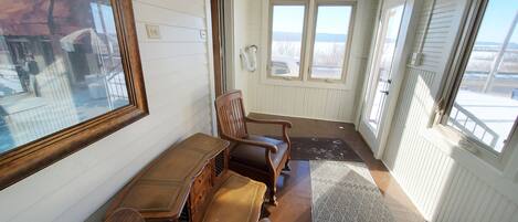 A narrow hallway with white paneled walls, a wooden bench, and a large window at the end.
