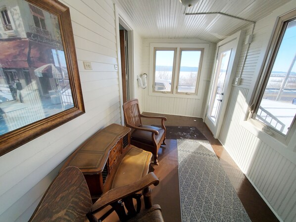 A narrow hallway with white paneled walls, a wooden bench, and a large window at the end.