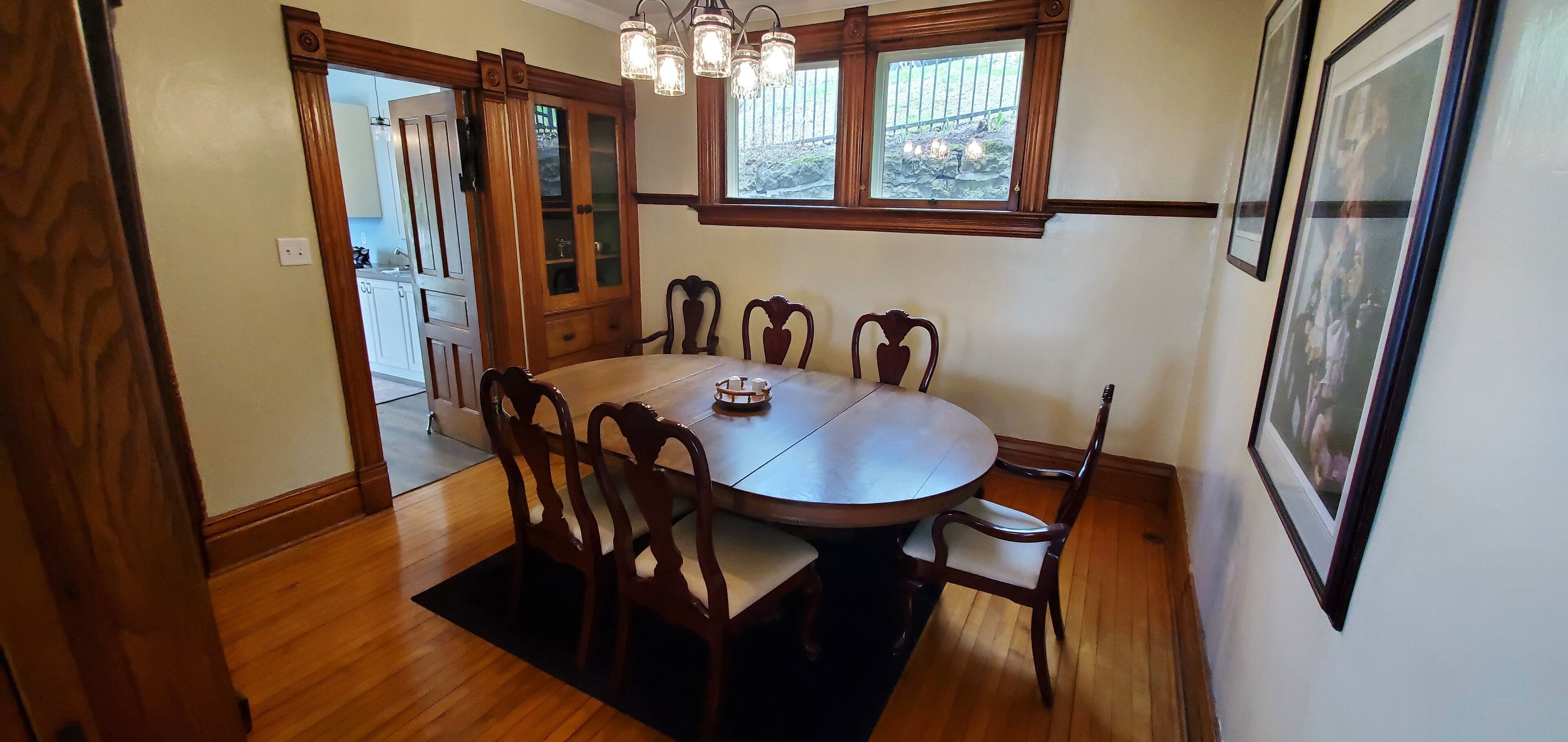 Une salle à manger avec une table ronde, six chaises, un lustre et une fenêtre donnant sur l’extérieur.