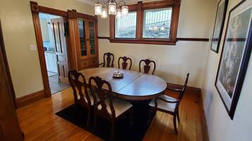 A dining room with a round table, six chairs, a chandelier, and a window with a view of the outdoors.