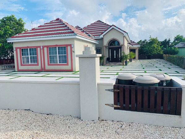 A residential area with two houses, one with a red-tiled roof and another with a black door. There is a paved walkway with green grass in between.