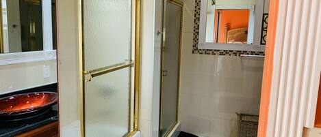 Une salle de bain avec une douche à parois de verre, un lavabo avec un receveur noir et un sol carrelé.