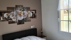 Une chambre dotée d’un grand lit, d’une œuvre d’art représentant des orchidées accrochée au mur, d’une table de chevet avec une lampe et d’une fenêtre offrant une vue agréable.