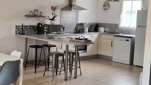 Une cuisine moderne dotée d’un îlot central, de tabourets de bar, d’une hotte en acier inoxydable et d’une fenêtre laissant entrer la lumière naturelle.