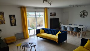 Un salon avec un canapé, une table à manger entourée de chaises, un téléviseur et des œuvres d’art accrochées aux murs.