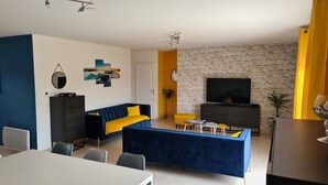 Un salon moderne avec un canapé bleu, une table basse et un téléviseur placés devant un mur en briques.